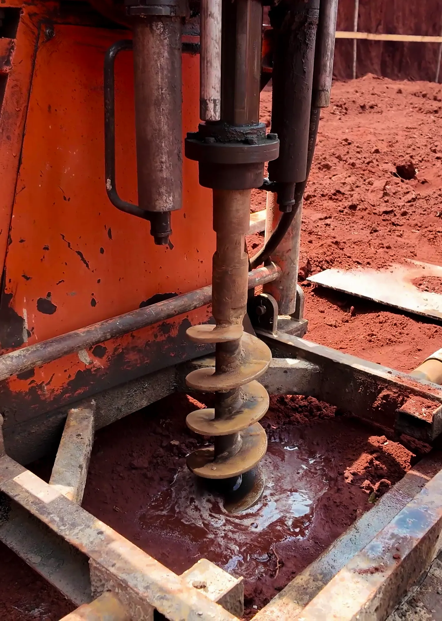 The auger biting into the wet red earth during geotechnical drilling