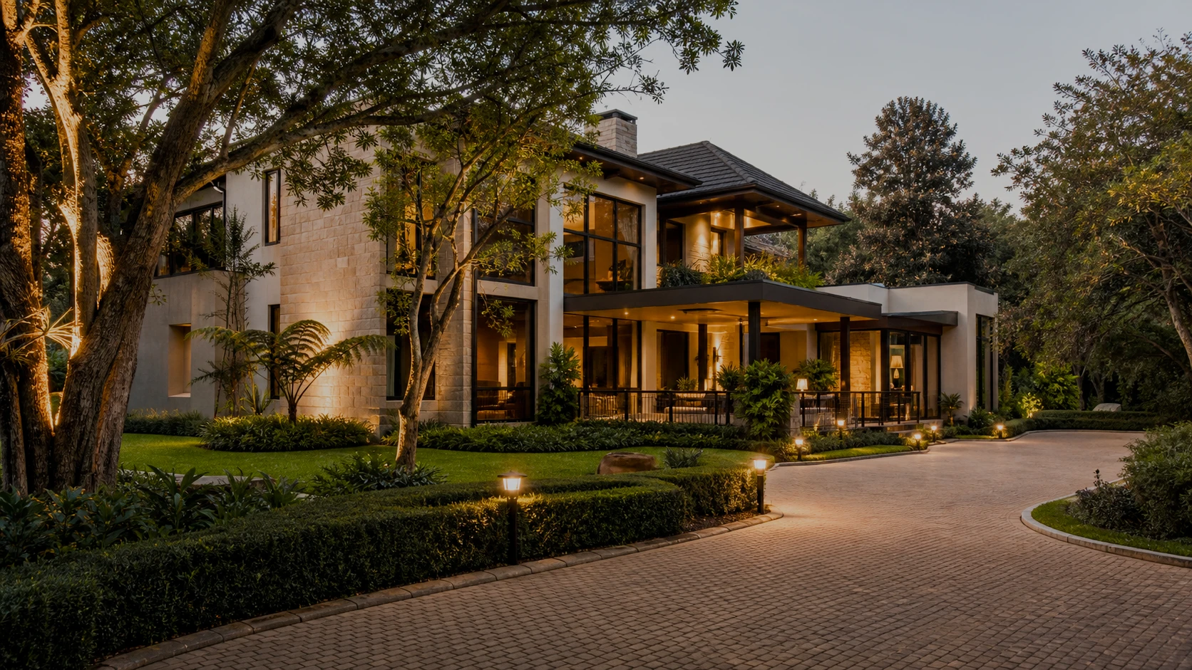 The paved drive and lit gardens of a Manor Ridge residence at dusk, concept render